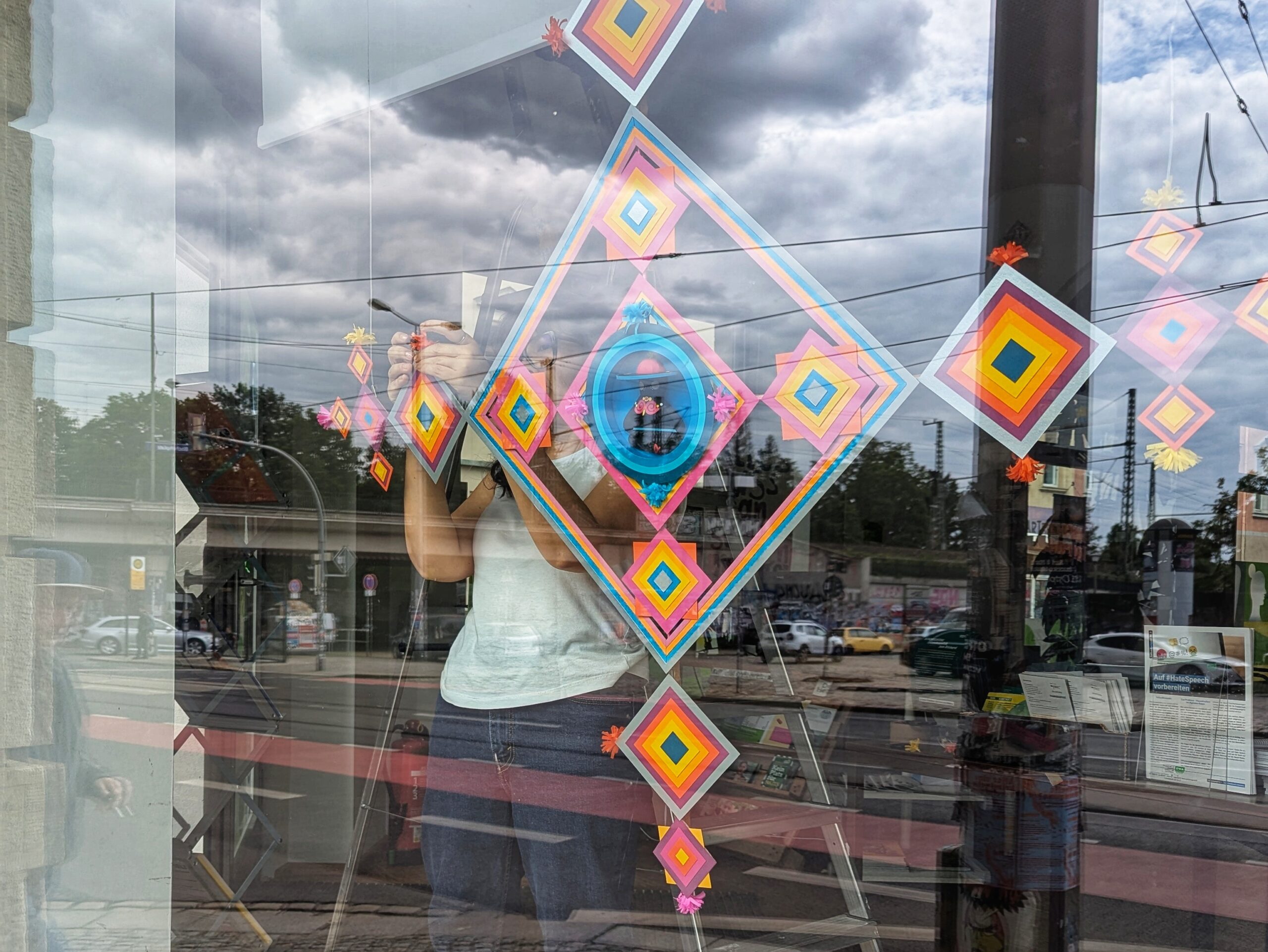 Die Künstlerin bela Alvarez baut ihre Arbeit im Kunstfenster der grünen Ecke auf. Dabei befestigt sie die Papierarbeit an den Galerieschnüren.